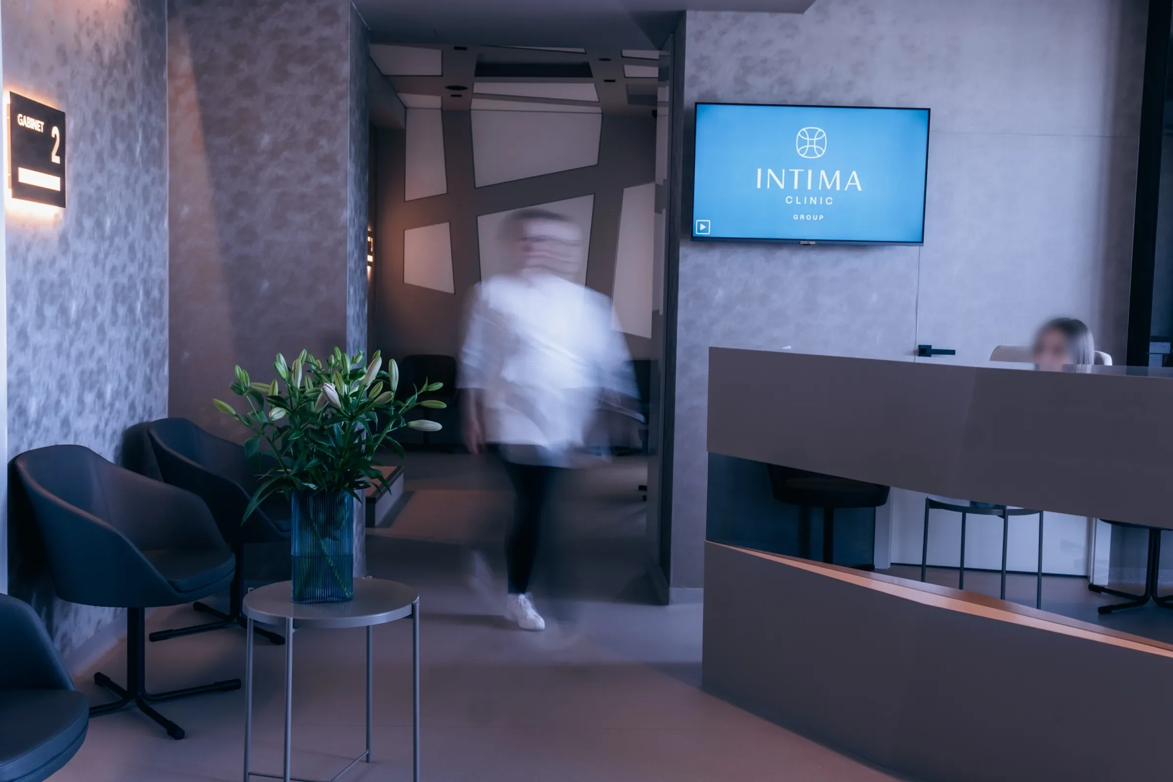Recepcja Intima Clinic z logo na ekranie nad ladą