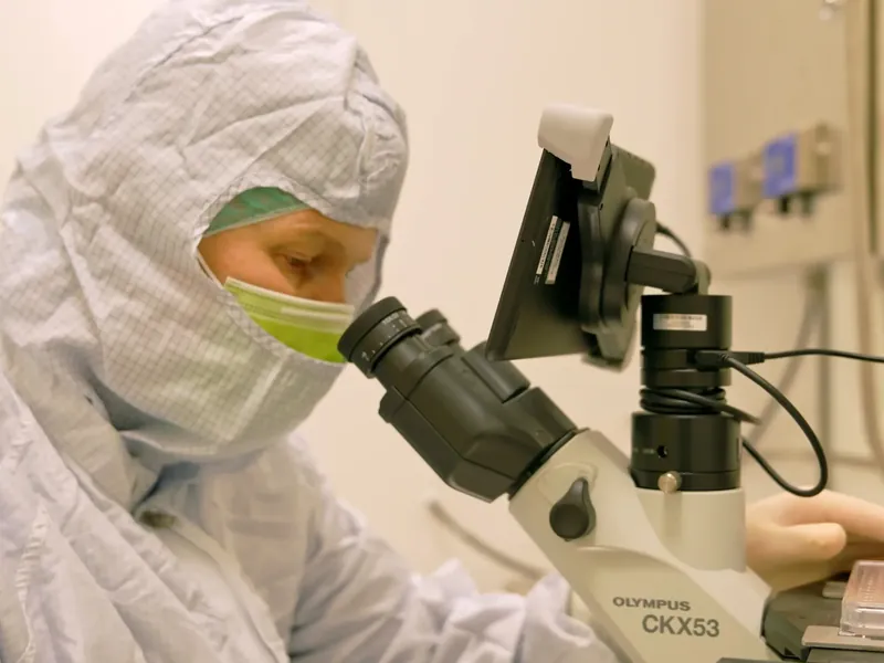 Naukowiec w kombinezonie i maseczce przy mikroskopie w laboratorium.