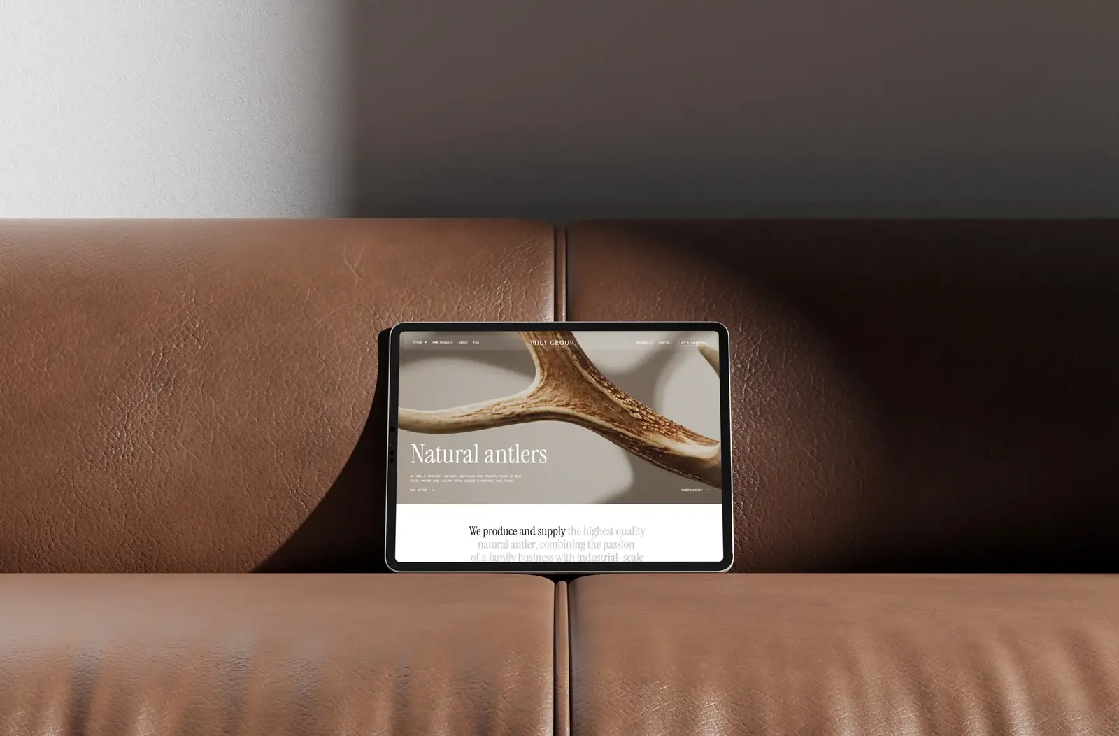 Strona milygroup.com na tablecie leżącym na skórzanej kanapie.